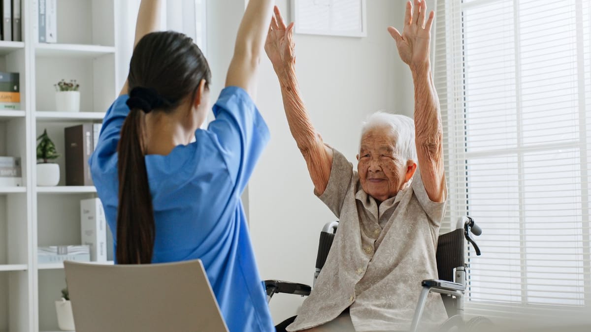 A care worker and an elderly woman raising their arms together during an exercise at home